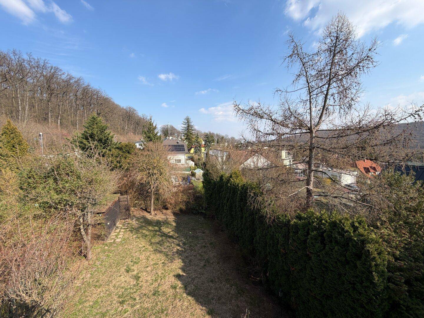Weitblick über den Garten und die umliegende grüne Landschaft mit bewaldeten Hügeln im Hintergrund.