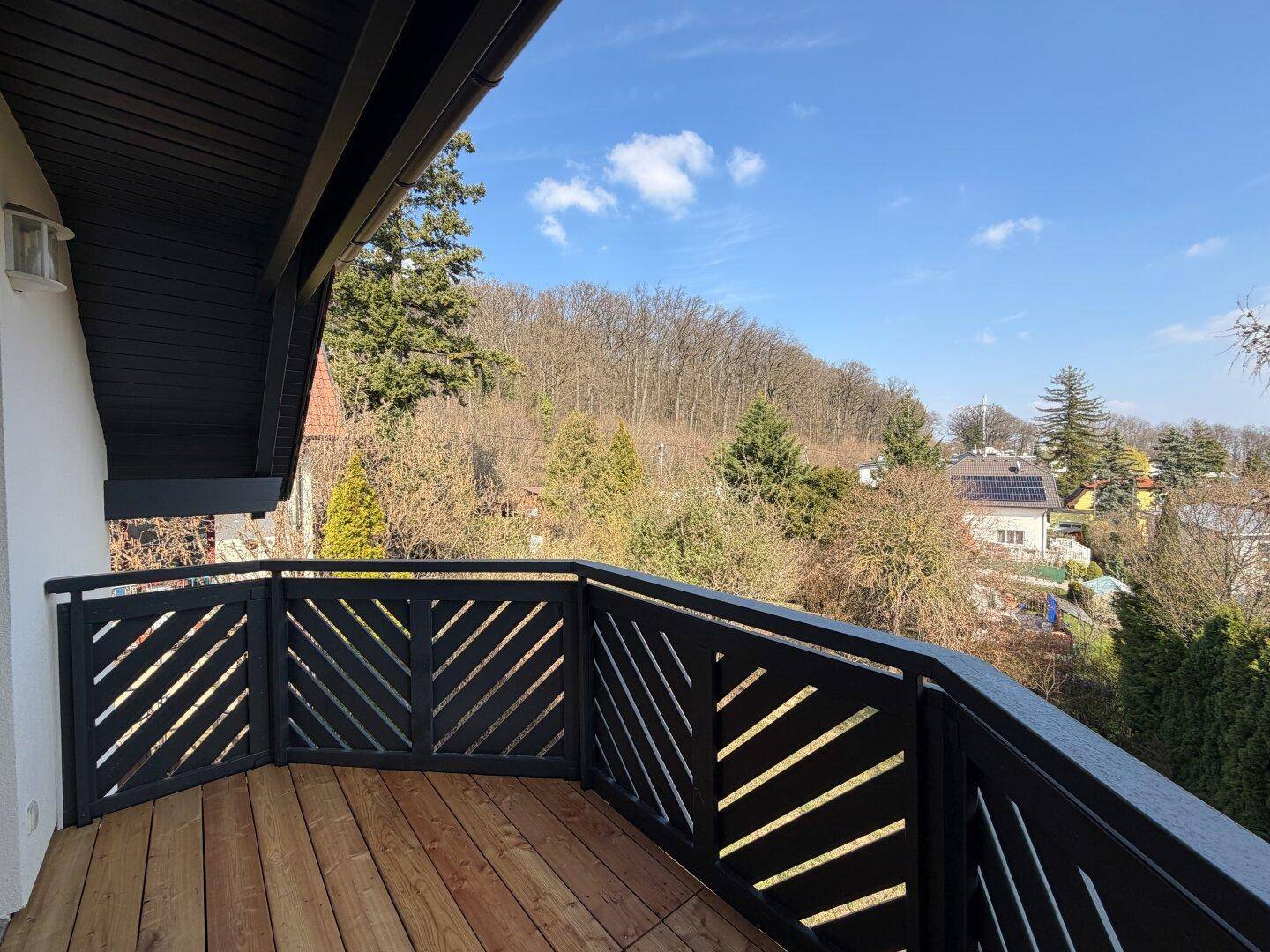 Sonniger Balkon mit Holzdielen und modernem Geländer, ideal zum Entspannen mit Blick auf die Landschaft.