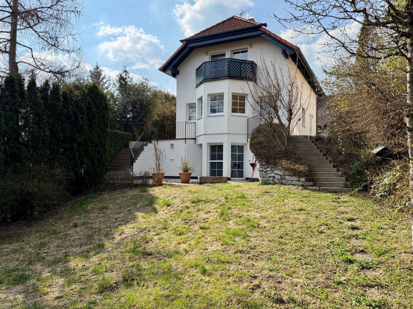 Rückseite des Hauses mit großem, leicht geneigtem Garten, Außentreppen und kleinem Balkon.