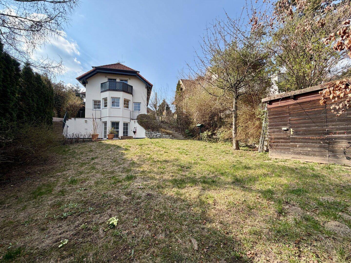Weitläufiger Gartenbereich hinter dem Haus mit Rasenfläche und einem praktischen Holzschuppen.