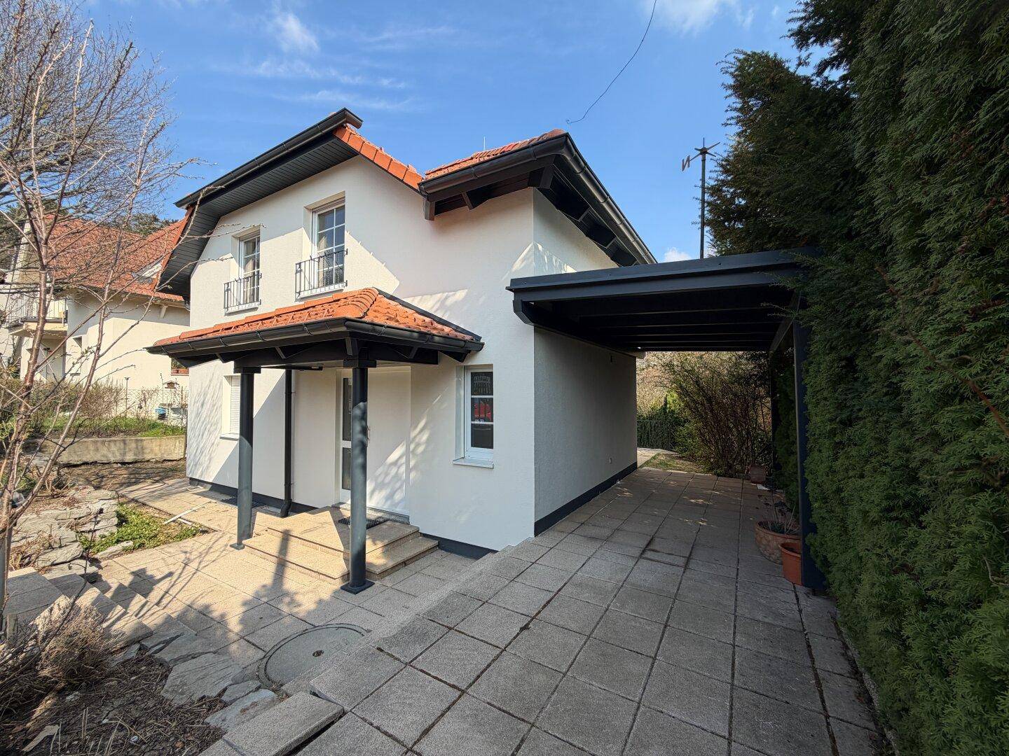 Seitenansicht des Hauses mit gepflasterter Einfahrt und einem überdachten Carport.