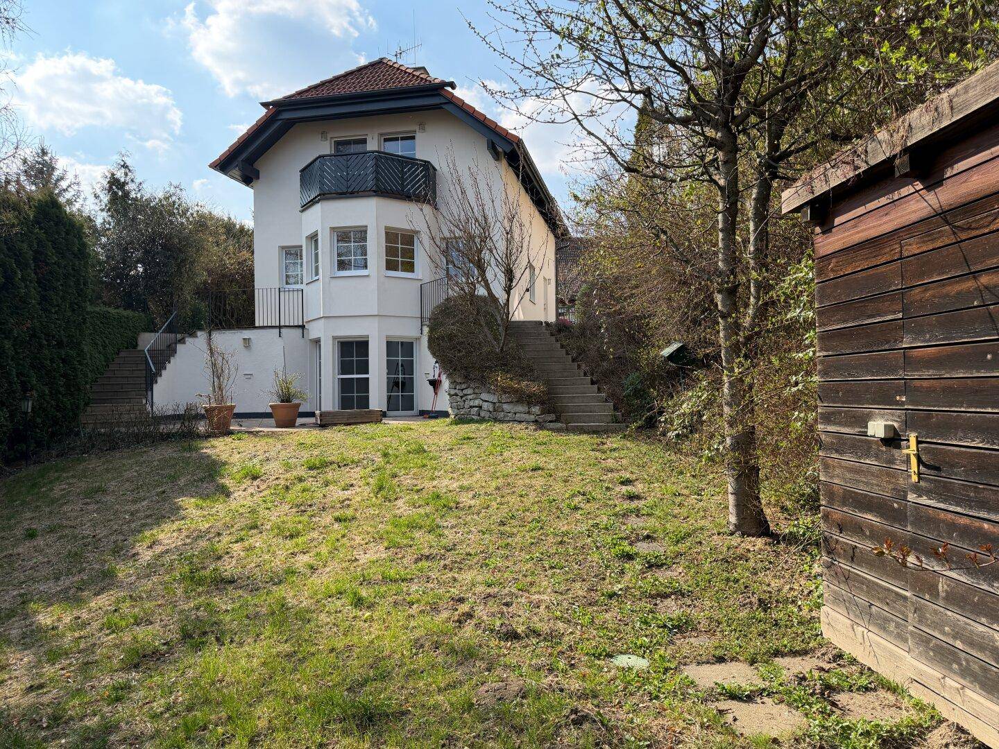 Gartenansicht des Hauses mit Rasenfläche, Außentreppen und einem rustikalen Holzschuppen.