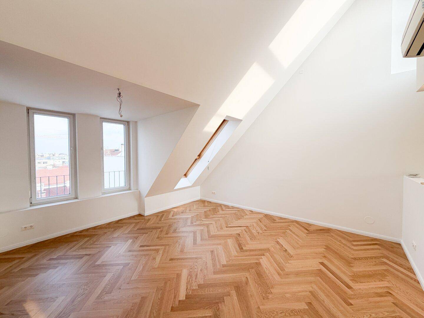 Lichtdurchfluteter Raum im Dachgeschoss mit schrägen Wänden und großen Fenstern.