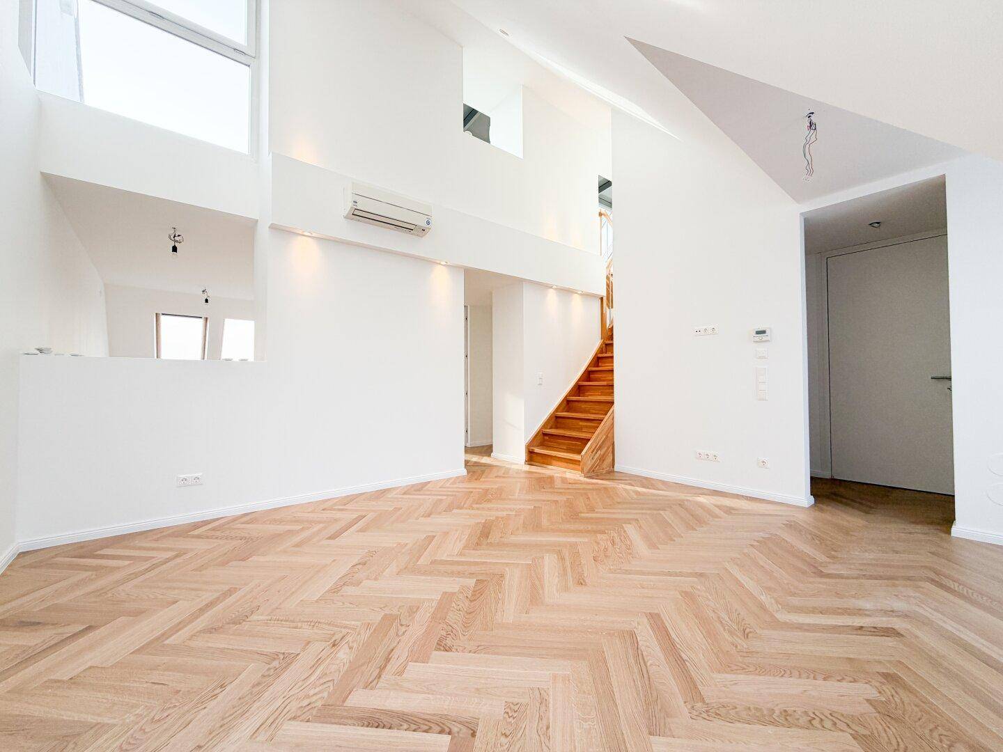 Großzügiges Wohnzimmer mit Fischgrätparkett, hohen Decken und viel Tageslicht.