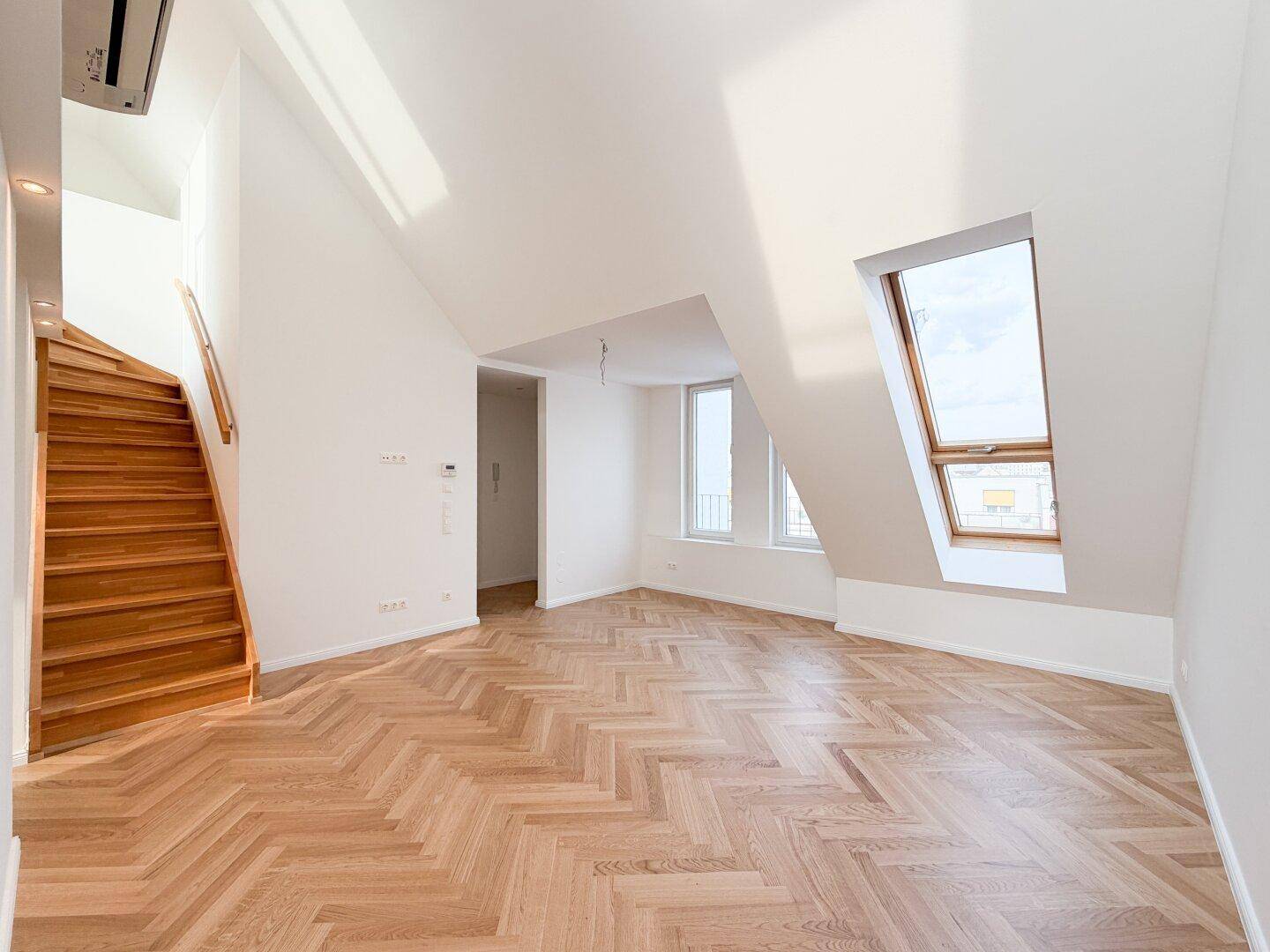 Heller Raum mit schrägen Decken, Dachfenstern und elegantem Fischgrätparkett.