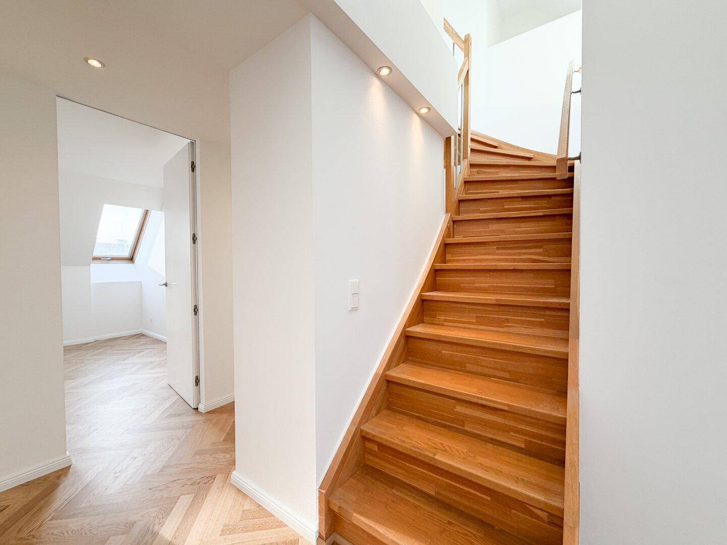 Elegante Holztreppe mit hellem Geländer, die die verschiedenen Ebenen verbindet.