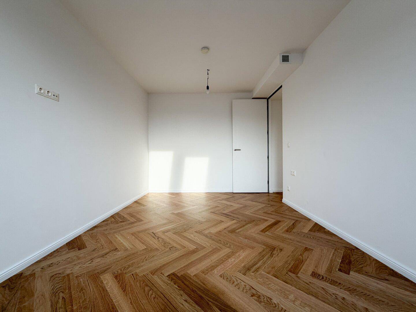 Heller Raum mit Fischgrätparkett und moderner weißer Tür, ideal als Schlafzimmer.