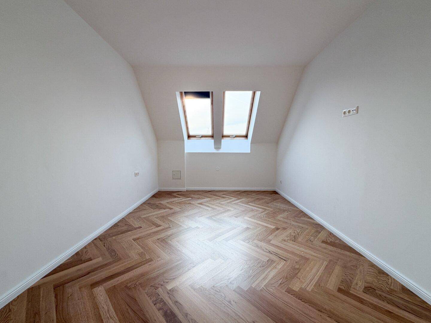 Ruhiges Schlafzimmer im Dachgeschoss mit zwei Dachfenstern und Fischgrätparkett.