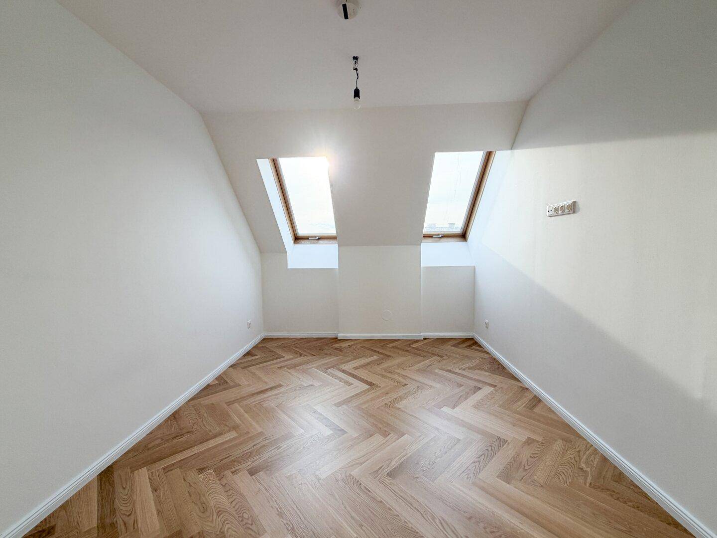 Gemütliches Schlafzimmer im Dachgeschoss mit zwei Dachfenstern und Fischgrätparkett.