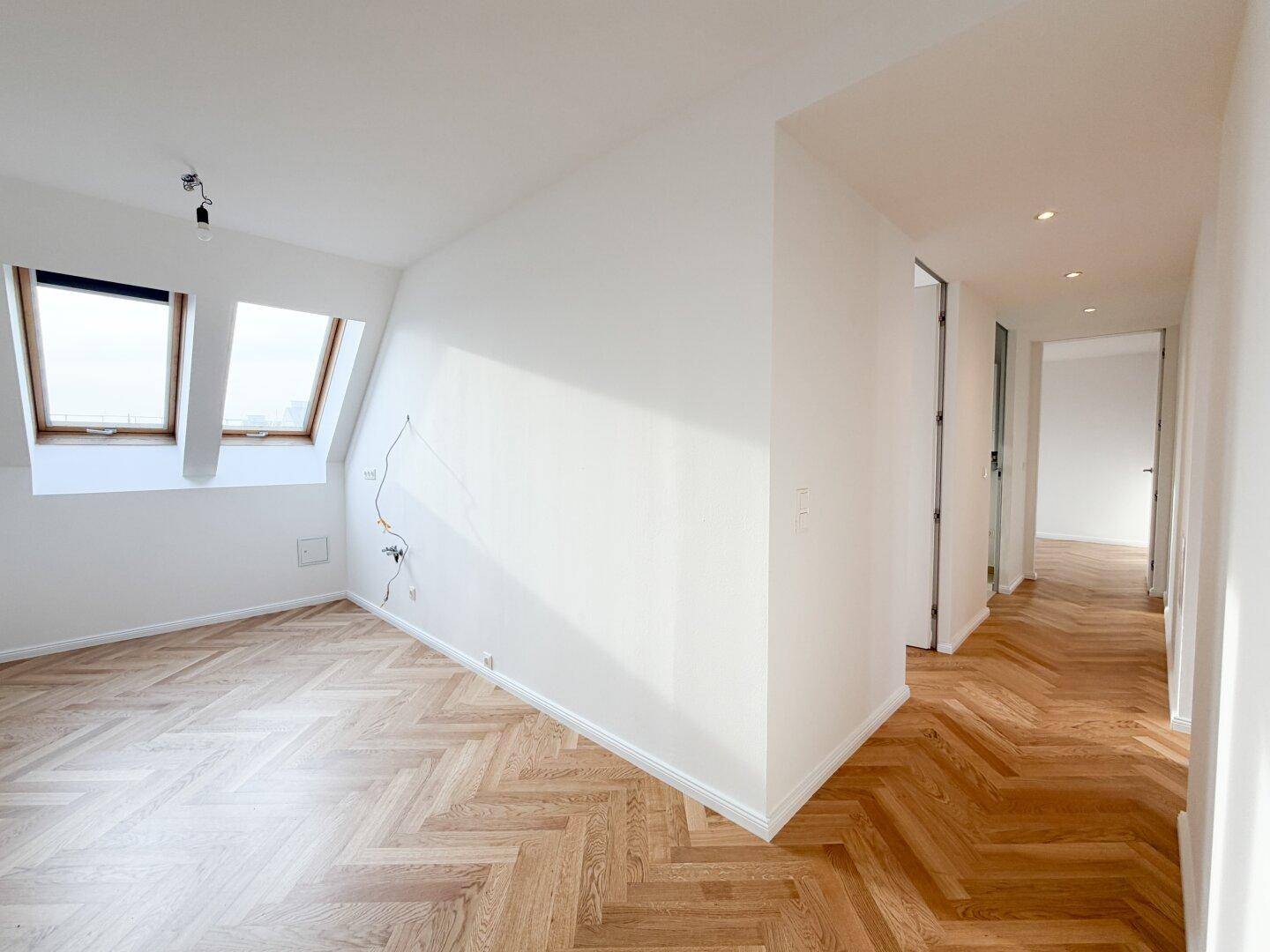 Helles Schlafzimmer mit Fischgrätparkett, Dachfenstern und Zugang zum Flur.