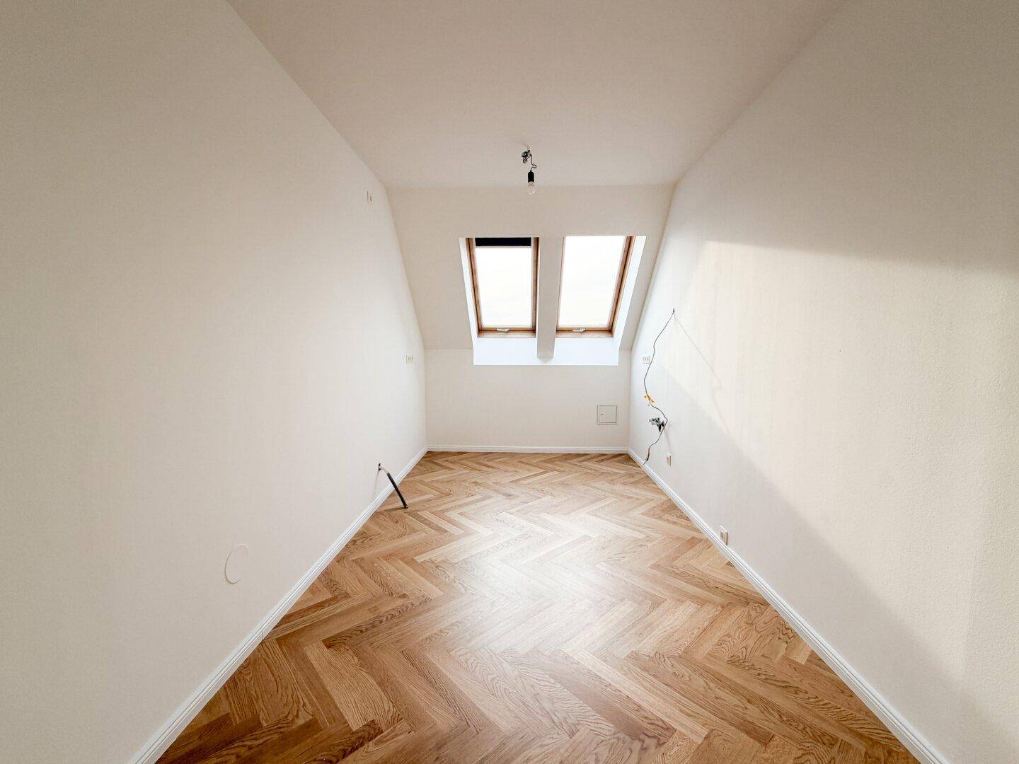 Gemütliches Schlafzimmer im Dachgeschoss mit zwei Dachfenstern und Fischgrätparkett.