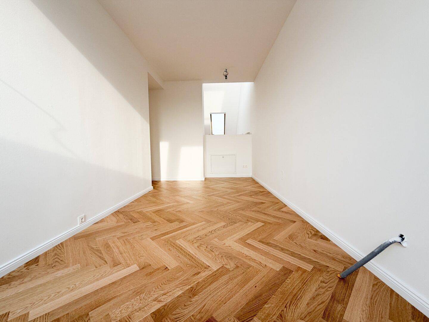 Langer, heller Raum mit Fischgrätparkett und einer Nische im Dachgeschoss.
