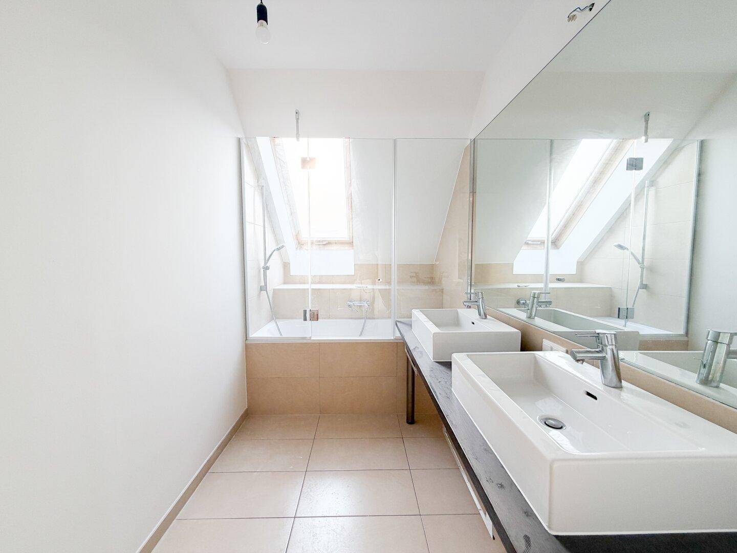 Modernes Badezimmer mit Doppelwaschbecken, Badewanne und Dachfenster.