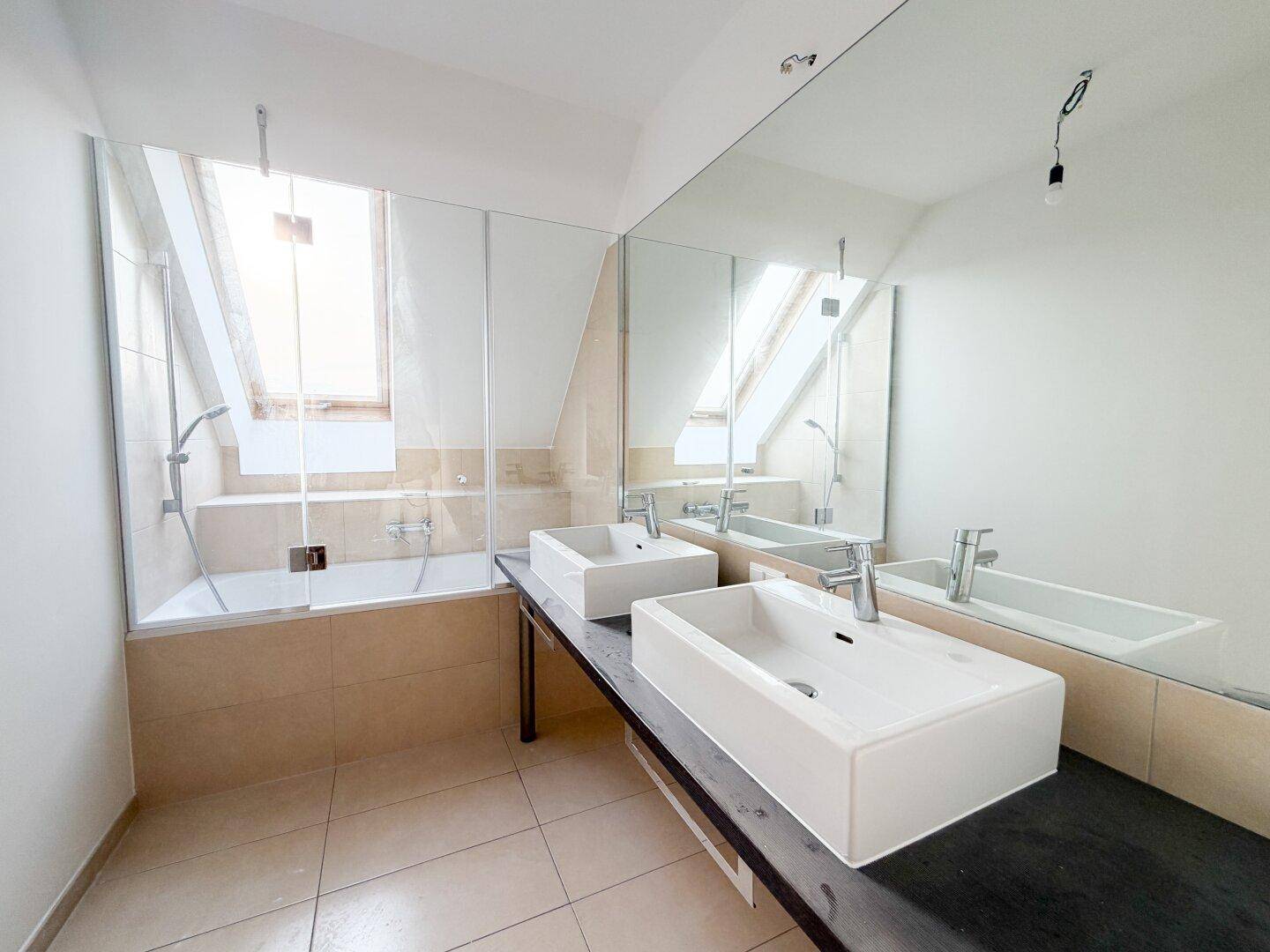 Helles Badezimmer mit Doppelwaschbecken, Badewanne und großem Spiegel.