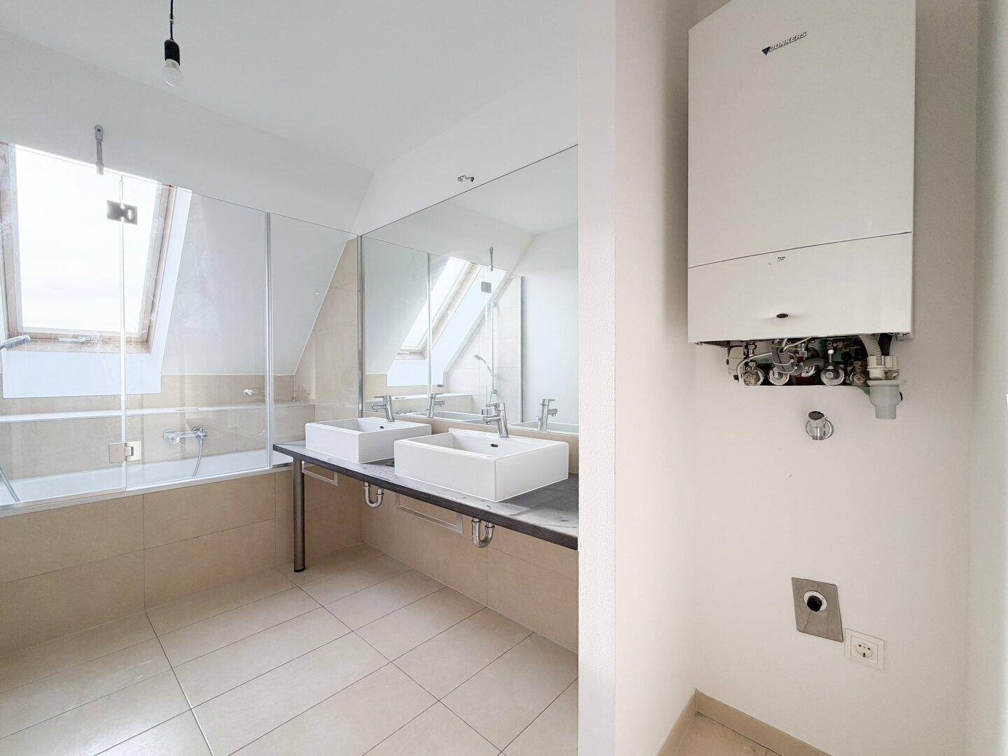 Badezimmer mit Doppelwaschbecken, Badewanne und sichtbarem Warmwasserbereiter.