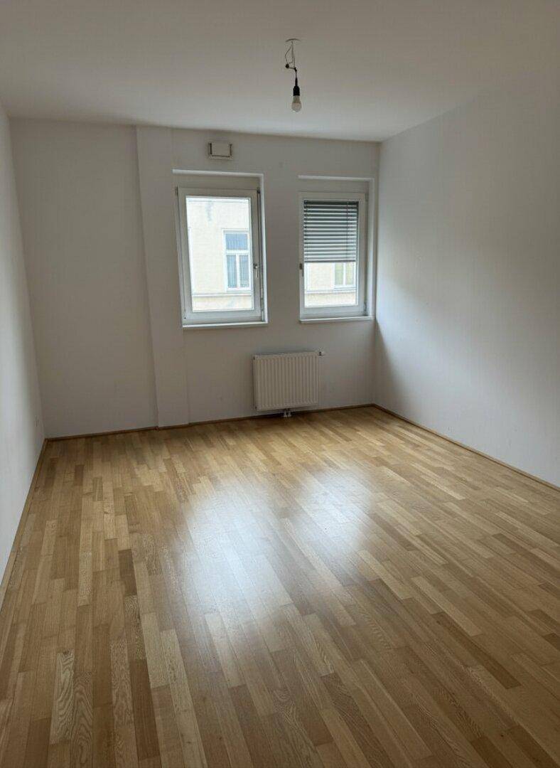 Helles Schlafzimmer mit Parkettboden und zwei Fenstern, bereit zur individuellen Gestaltung.