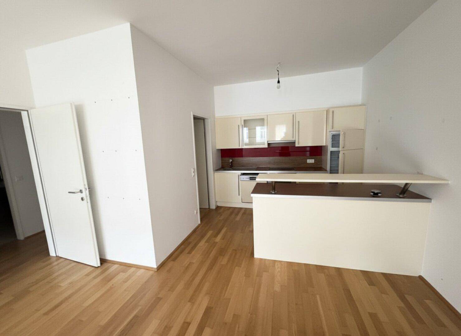 Einbauküche mit beigefarbenen Schränken, roter Rückwand und integrierter Frühstücksbar.