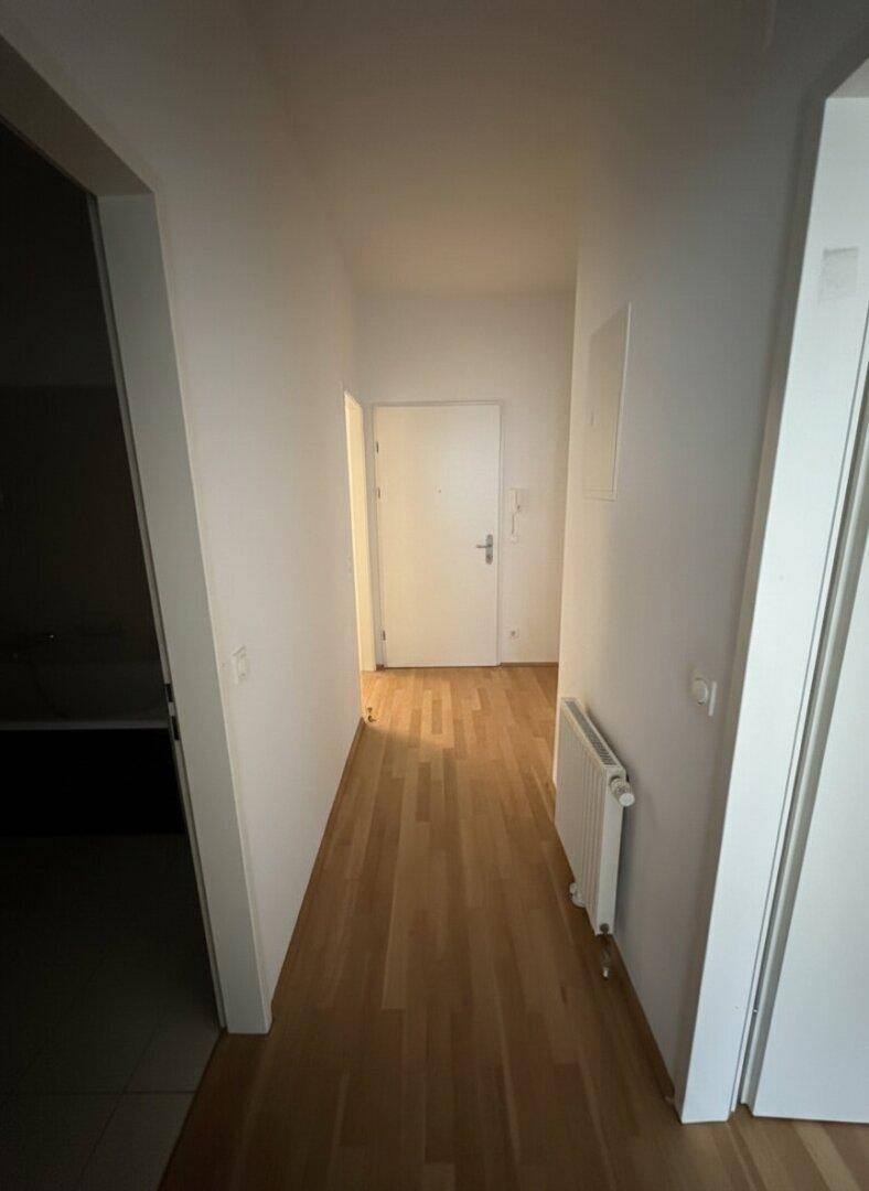 Heller Flur mit Parkettboden und weiß gestrichenen Wänden, der zu weiteren Räumen führt.