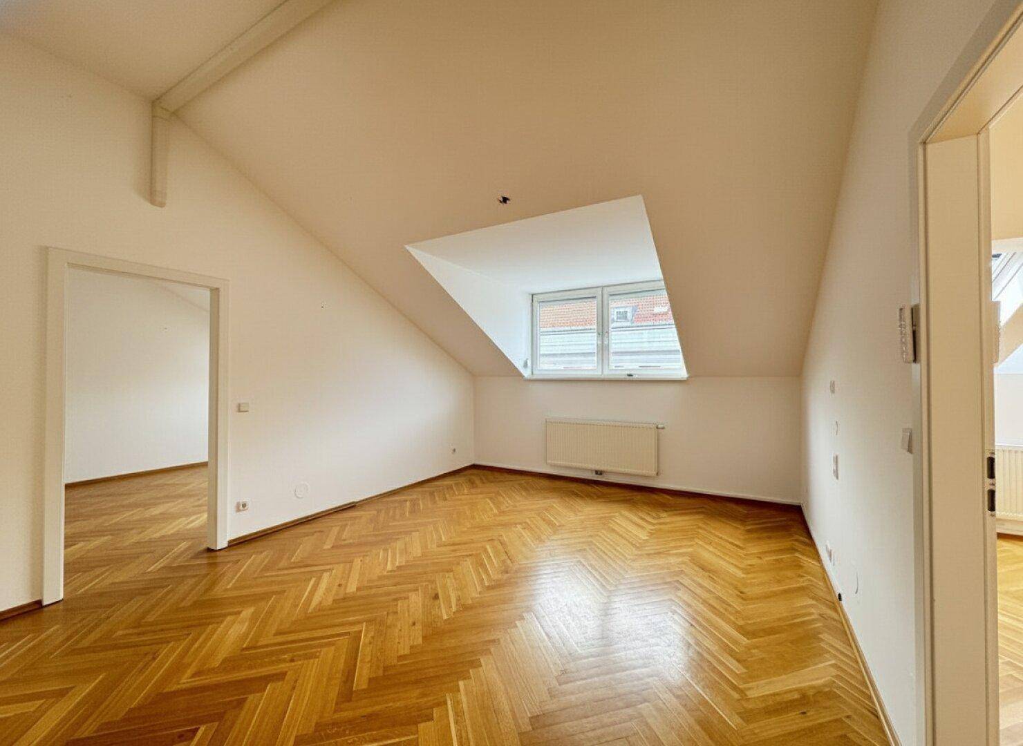 Schlafzimmer im Dachgeschoss mit schräger Decke, Parkettboden und einem Fenster für natürliches Licht.
