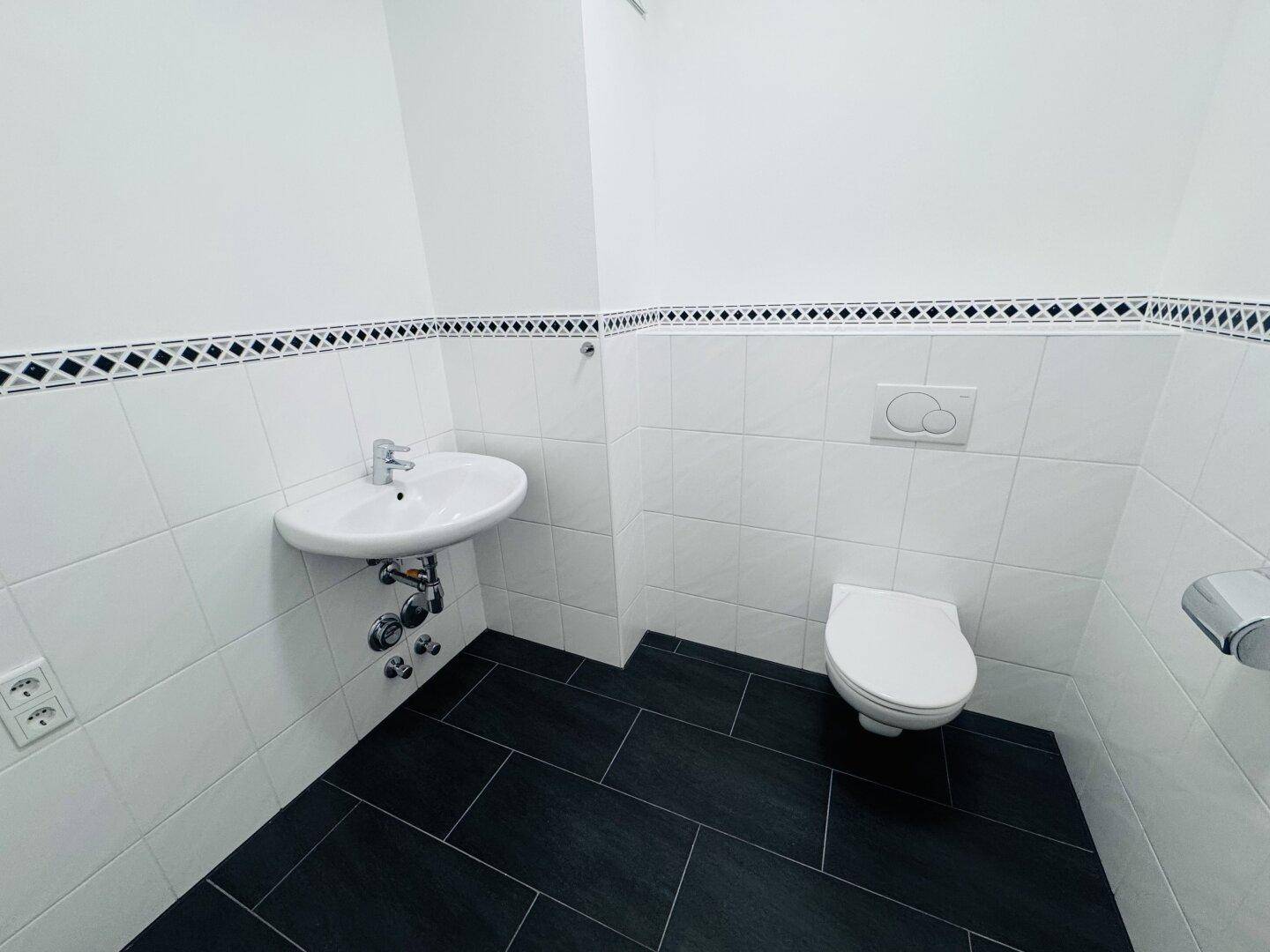 Separates Gäste-WC mit Waschtisch und Wand-WC, ausgestattet mit dunklen Bodenfliesen.