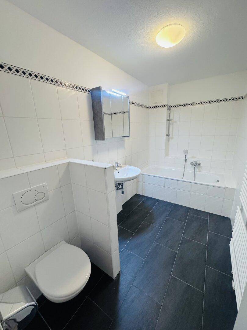 Modernes Badezimmer mit Badewanne, WC und Waschtisch, ausgestattet mit dunklen Bodenfliesen.