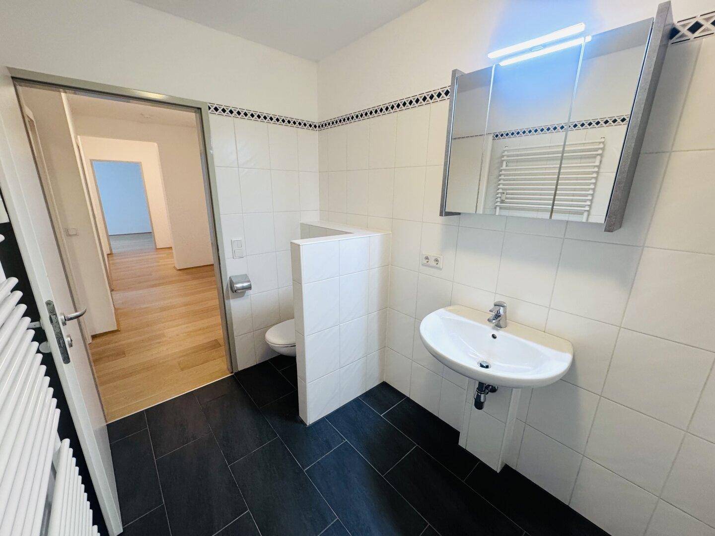Helles Badezimmer mit dunklen Bodenfliesen, weißer Wandverkleidung und modernem Waschtisch.