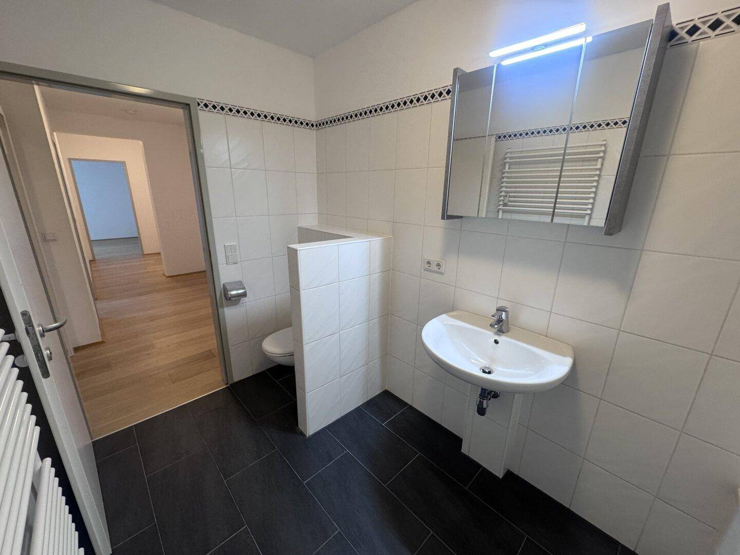 Funktionales Badezimmer mit Waschtisch, WC und Spiegelschrank, hell gefliest und gut beleuchtet.