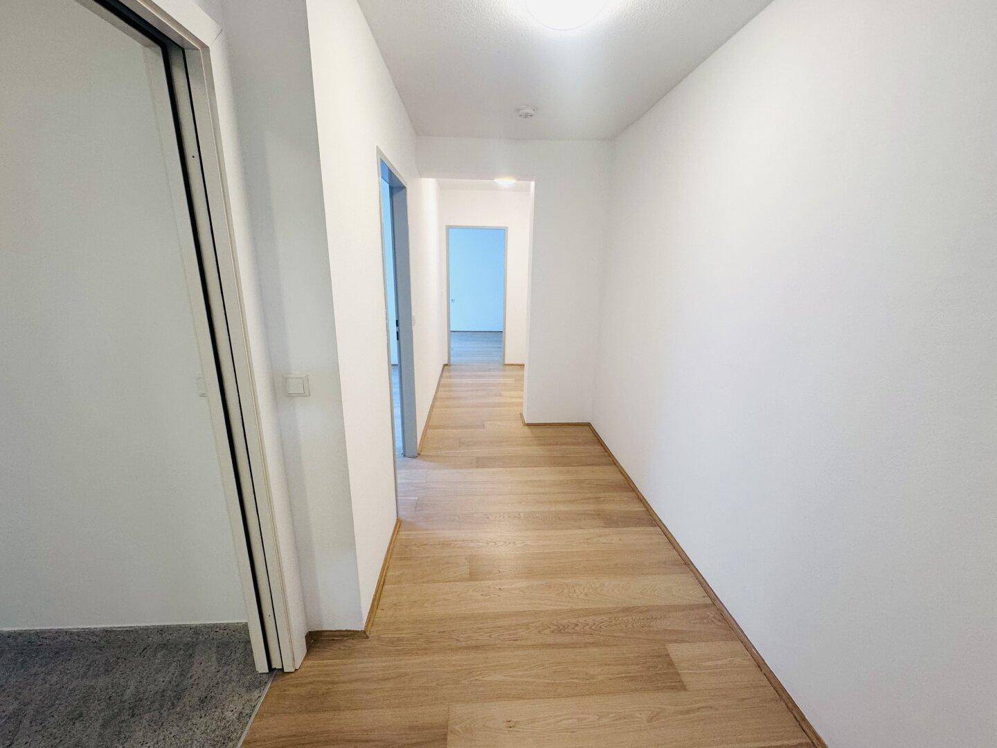 Geräumiger Flur mit Holzboden und weiß gestrichenen Wänden, der die Wohnbereiche verbindet.