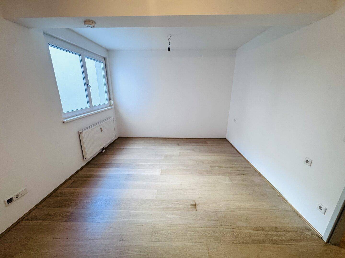 Helles Zimmer mit Parkettboden und großem Fenster, ideal als Schlaf- oder Arbeitszimmer.