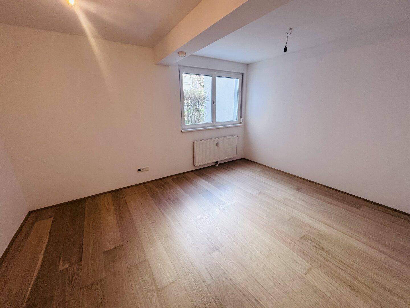 Leeres Schlafzimmer mit hellem Parkettboden und Fenster, bereit zur individuellen Gestaltung.