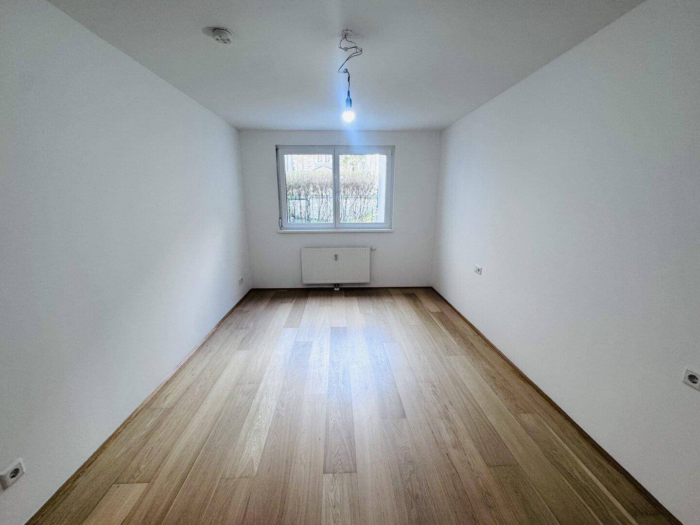 Helles Schlafzimmer mit Parkettboden und Fenster, das viel Tageslicht hereinlässt.