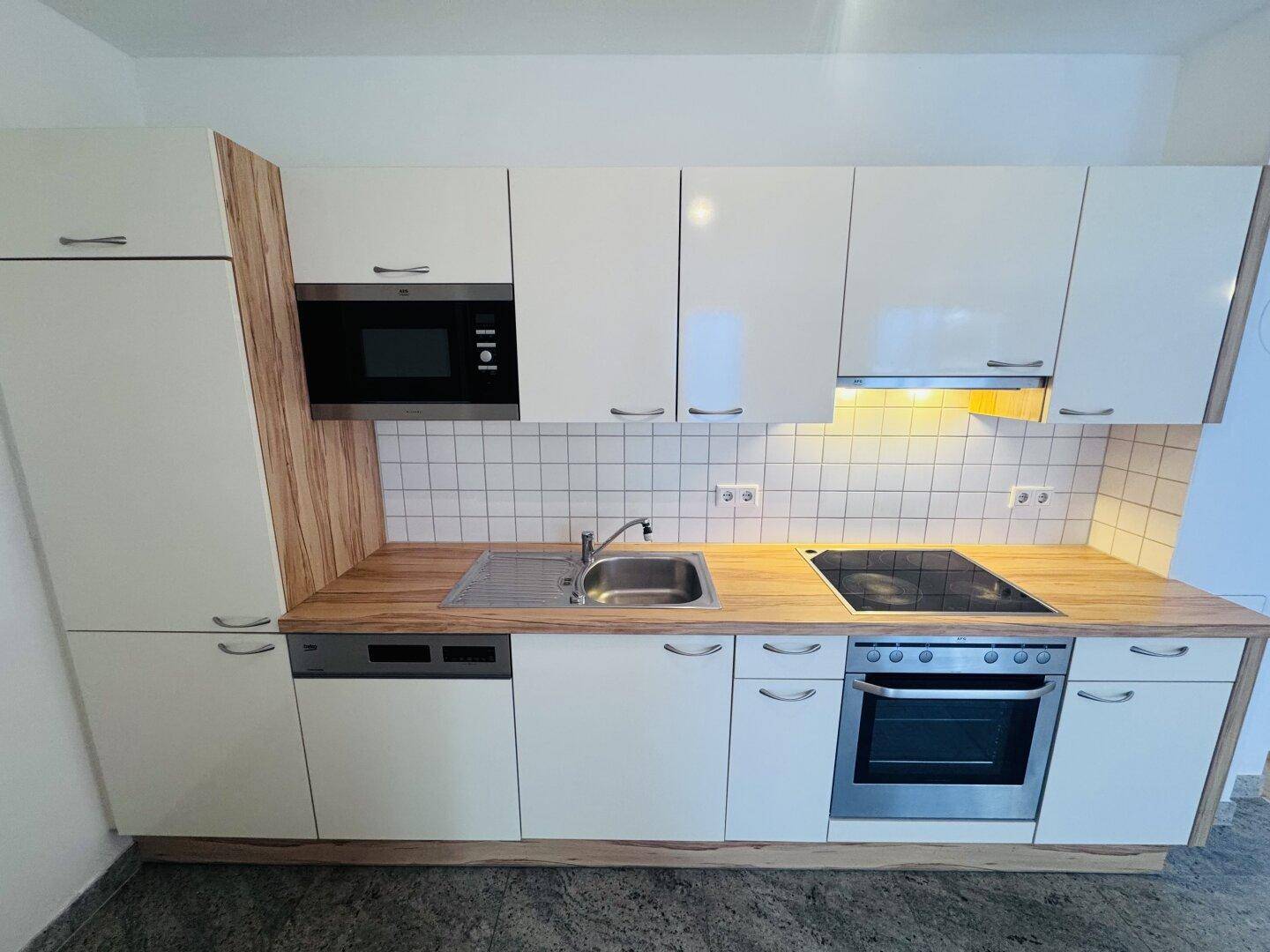 Moderne Einbauküche mit weißen Schränken, Holzarbeitsplatte und integrierten Geräten.