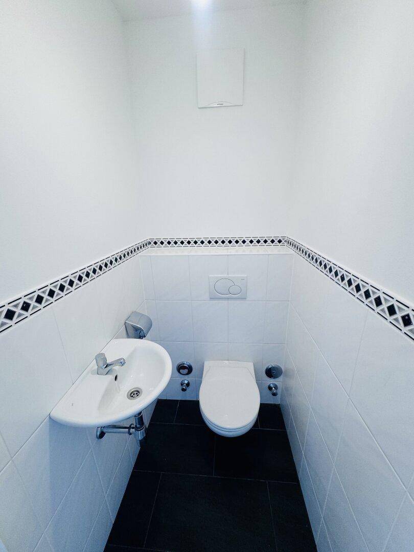 Separates WC mit Waschbecken und weißen Wandfliesen.