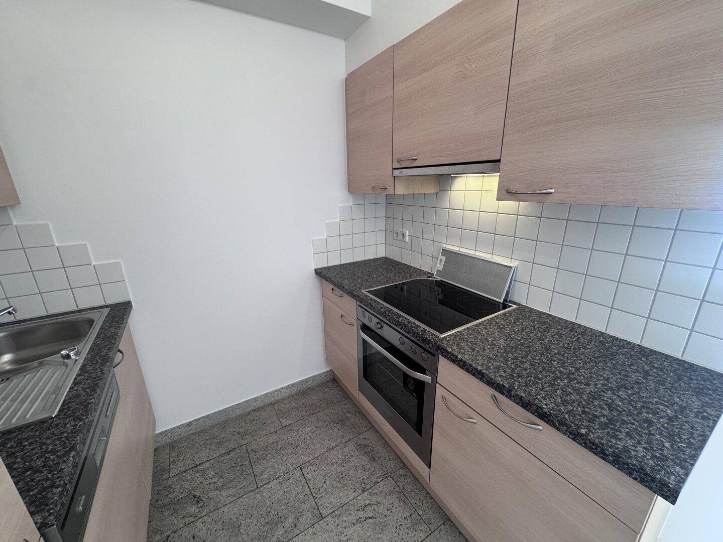 Funktionale Küche mit hellen Holzschränken, Granitarbeitsplatte und Kochfeld.