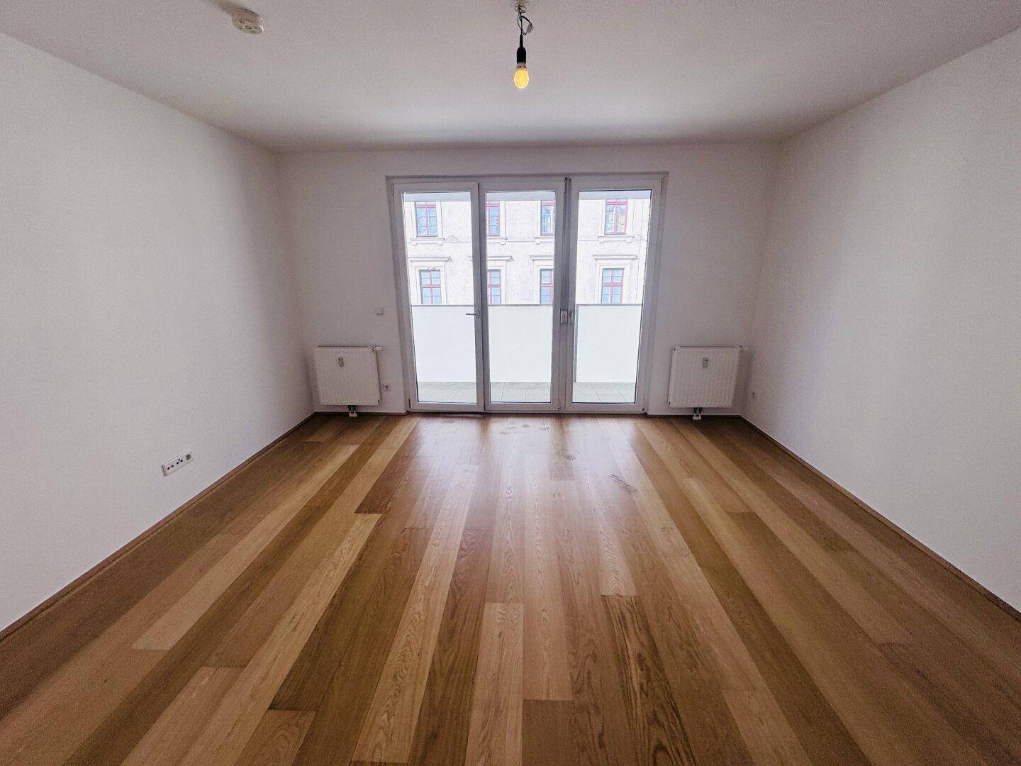 Geräumiges, leeres Zimmer mit Holzparkett und großen Fenstertüren.