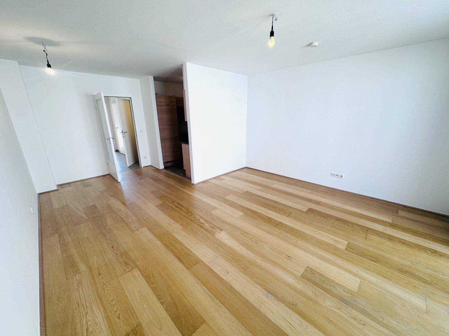 Geräumiges, leeres Zimmer mit hellem Holzparkett und weißen Wänden.