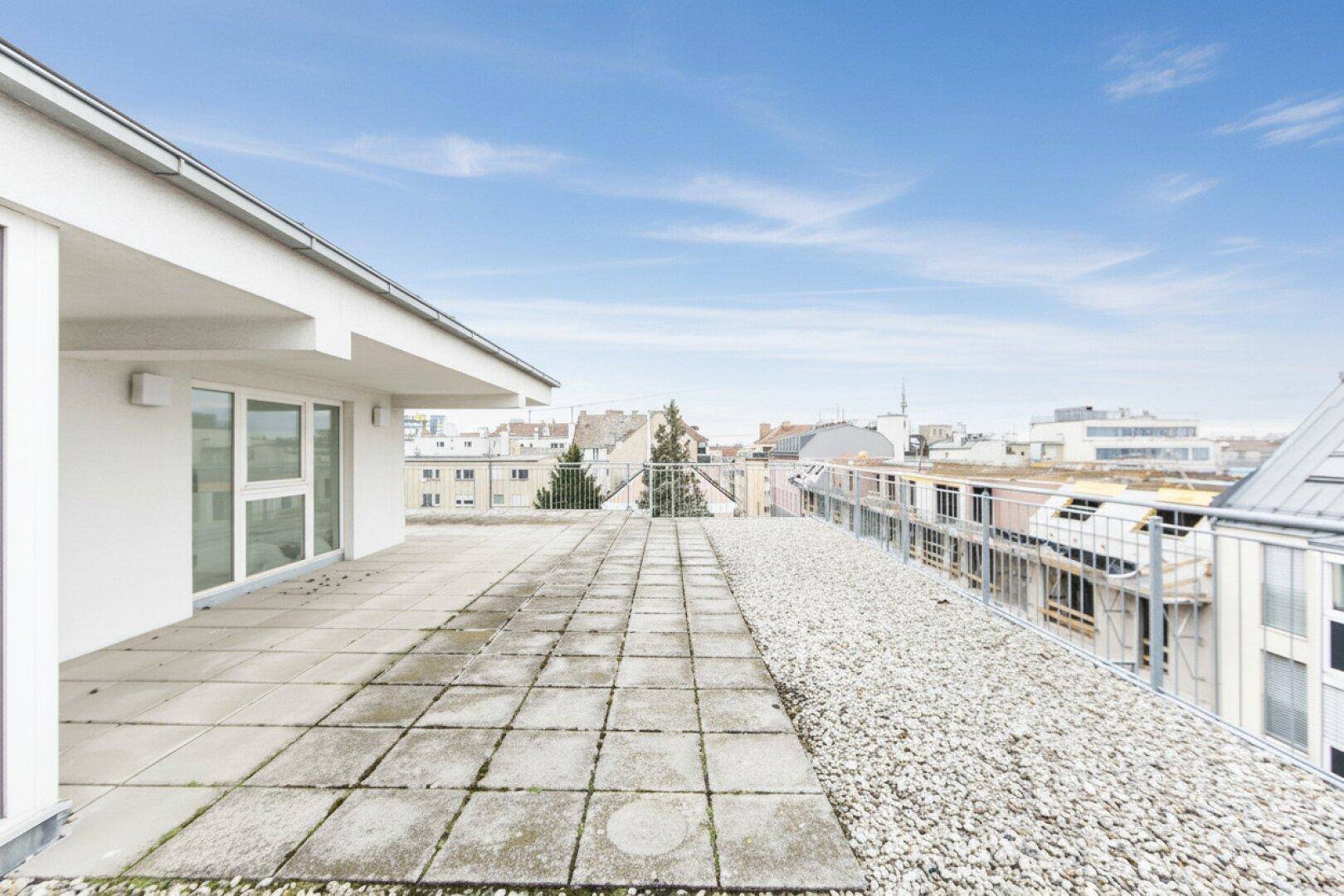 Große Dachterrasse mit Fliesen und Kies, bietet einen weiten Blick über die städtische Umgebung und viel Sonnenlicht.