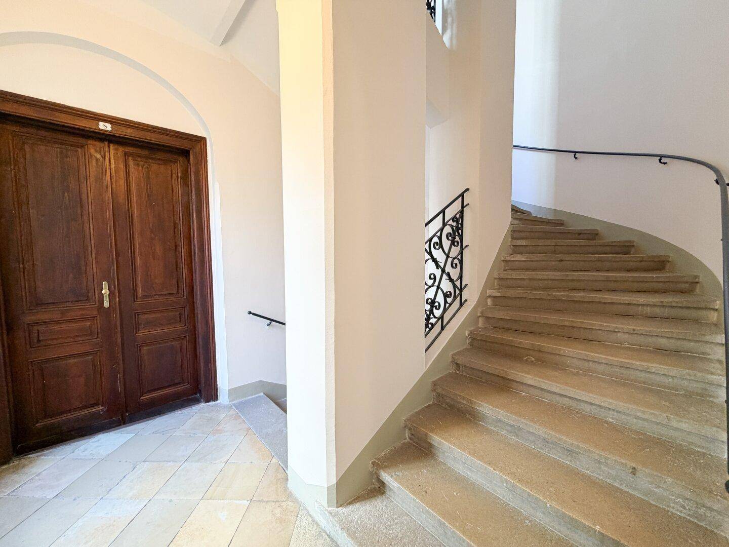 Geschwungene Steintreppe mit schmiedeeisernem Geländer in einem historischen Gebäude.