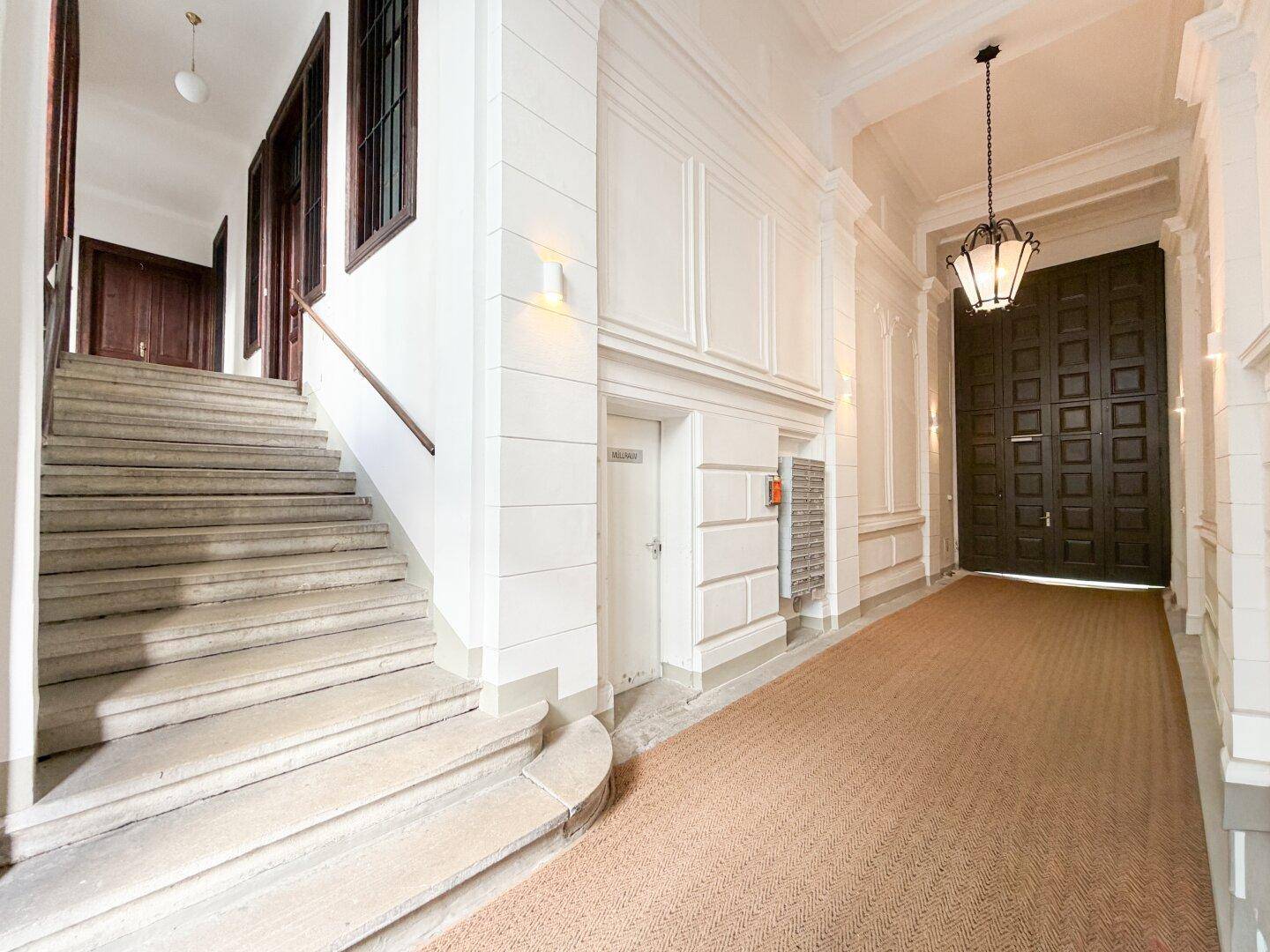 Eleganter Eingangsbereich mit Steintreppe, Stuckdecken und einem langen Teppichläufer.