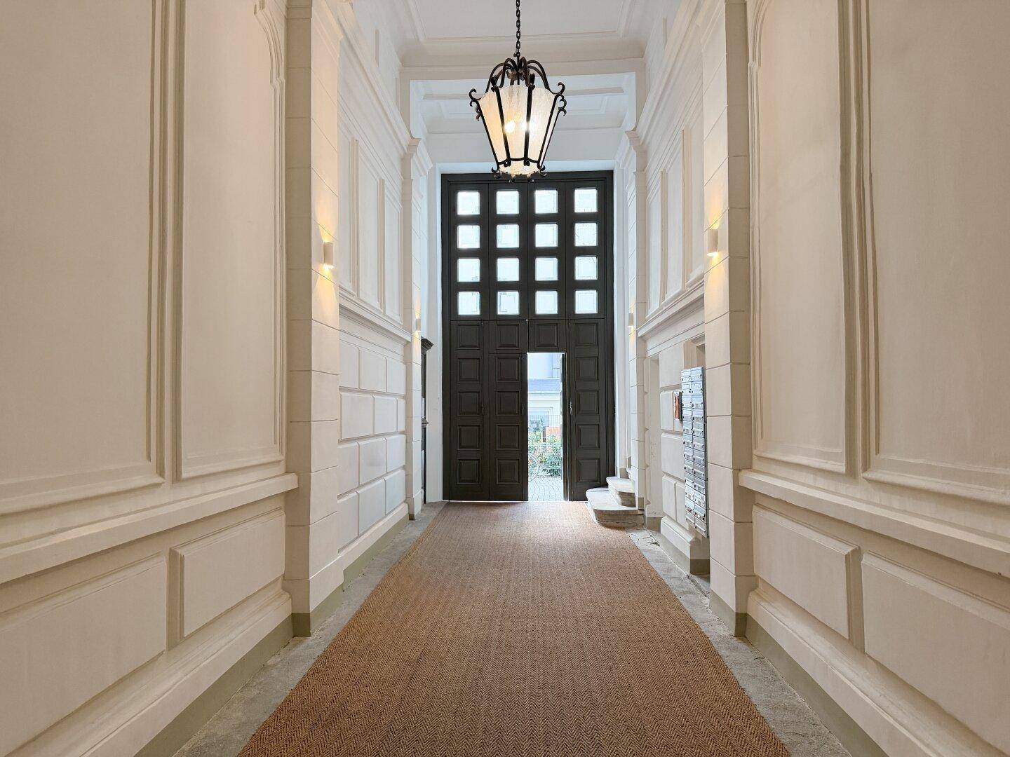 Langer, heller Flur mit hohen Decken, dekorativen Wandpaneelen und einer großen Eingangstür.