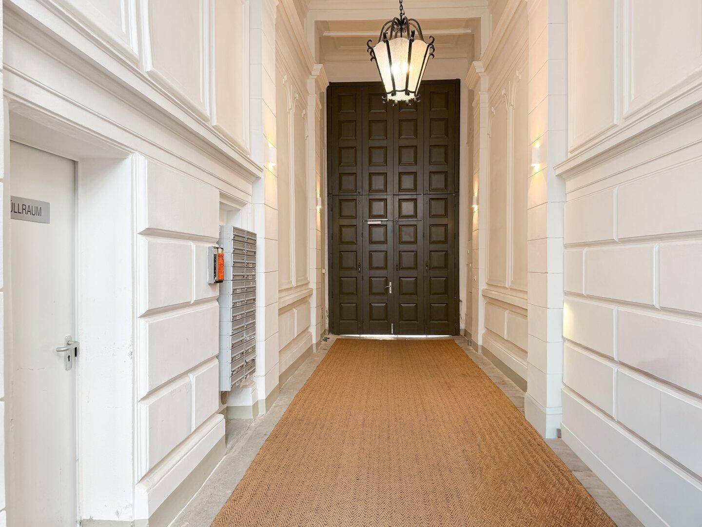 Stilvoller Eingangsbereich mit klassischer Beleuchtung, hohen Wänden und einem Briefkastenbereich.