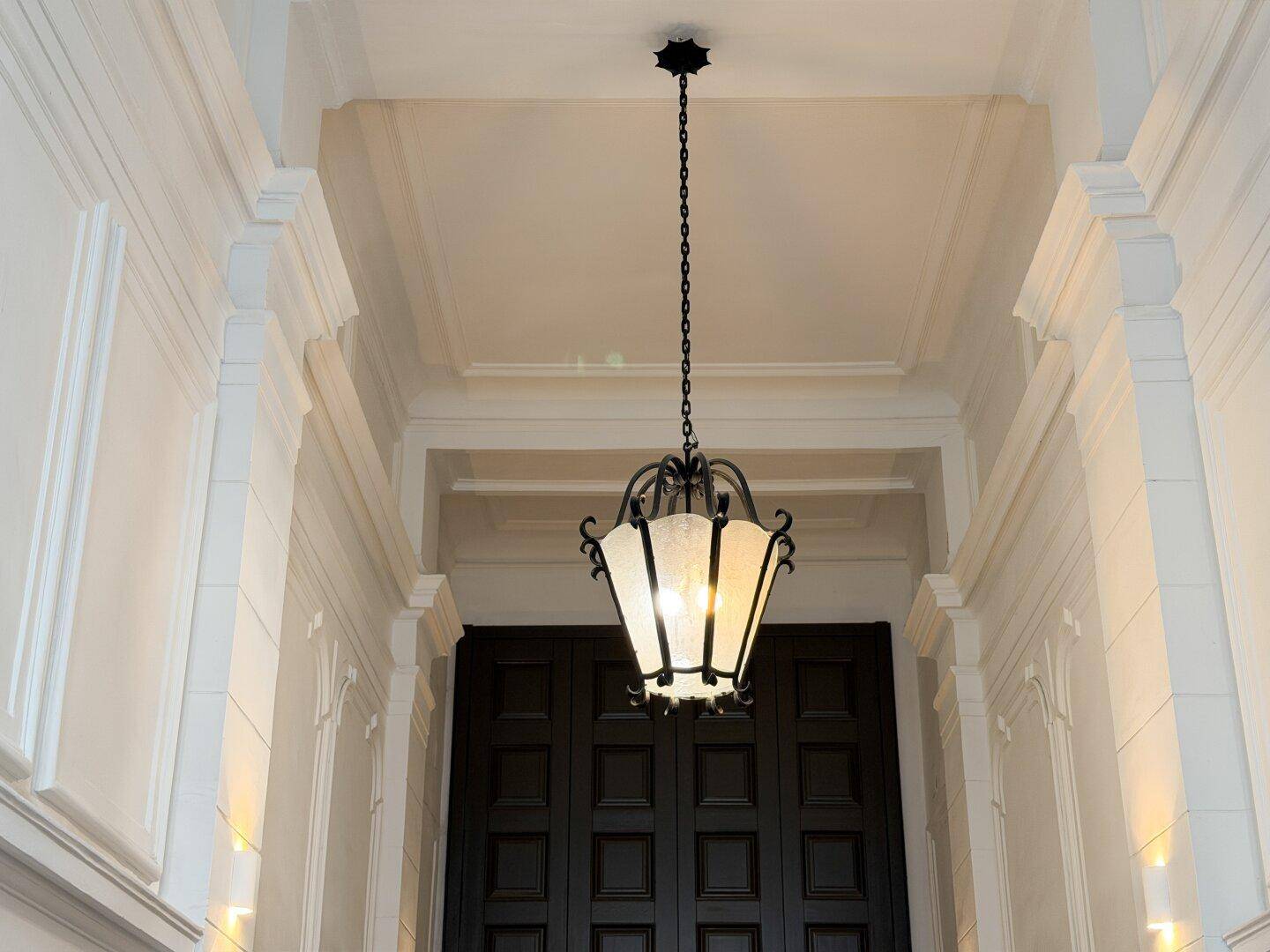 Detailaufnahme der hohen Decke mit Stuckelementen und einer eleganten Hängelampe im Eingangsbereich.