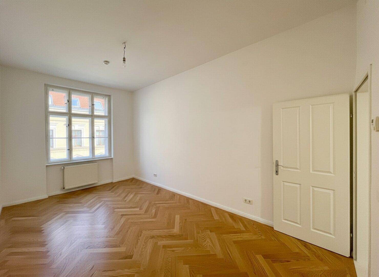 Geräumiges Zimmer mit neuem Fischgrätparkett, weißen Wänden und viel Tageslicht.