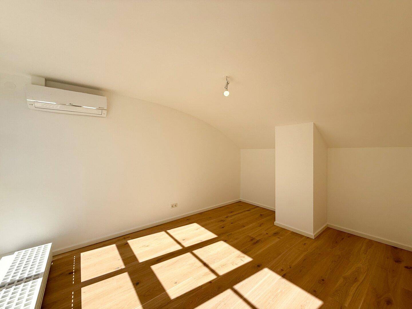 Lichtdurchfluteter Raum mit Holzboden, Klimaanlage und Dachschräge.