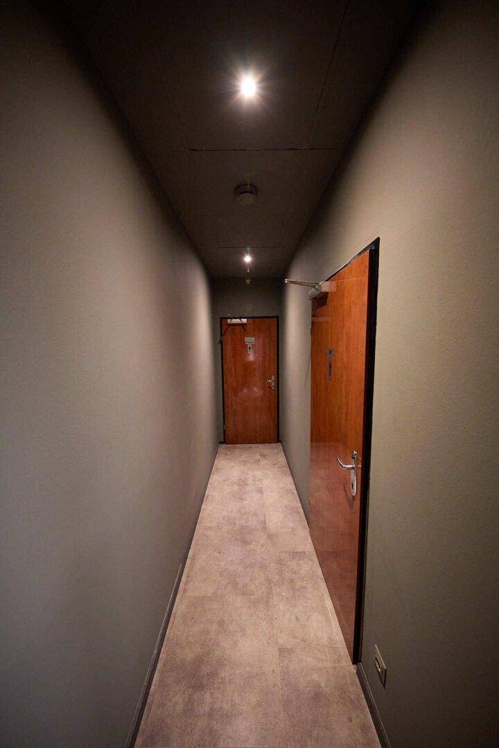 Langer Flur mit Holztüren und Fliesenboden, beleuchtet von Deckenspots.
