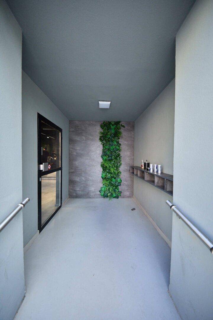 Heller Eingangsbereich mit Rampe, Handläufen und einer vertikalen Pflanzenwand.