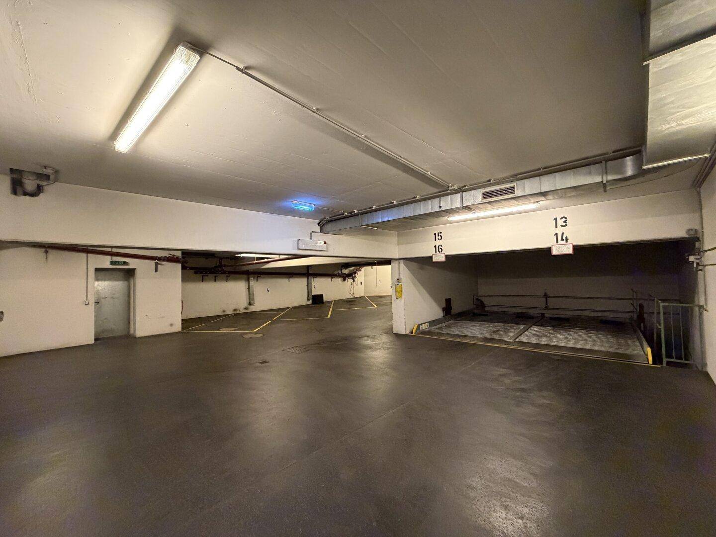Helle Tiefgarage mit vielen Parkplätzen und einem mechanischen Parksystem für zusätzliche Fahrzeuge.