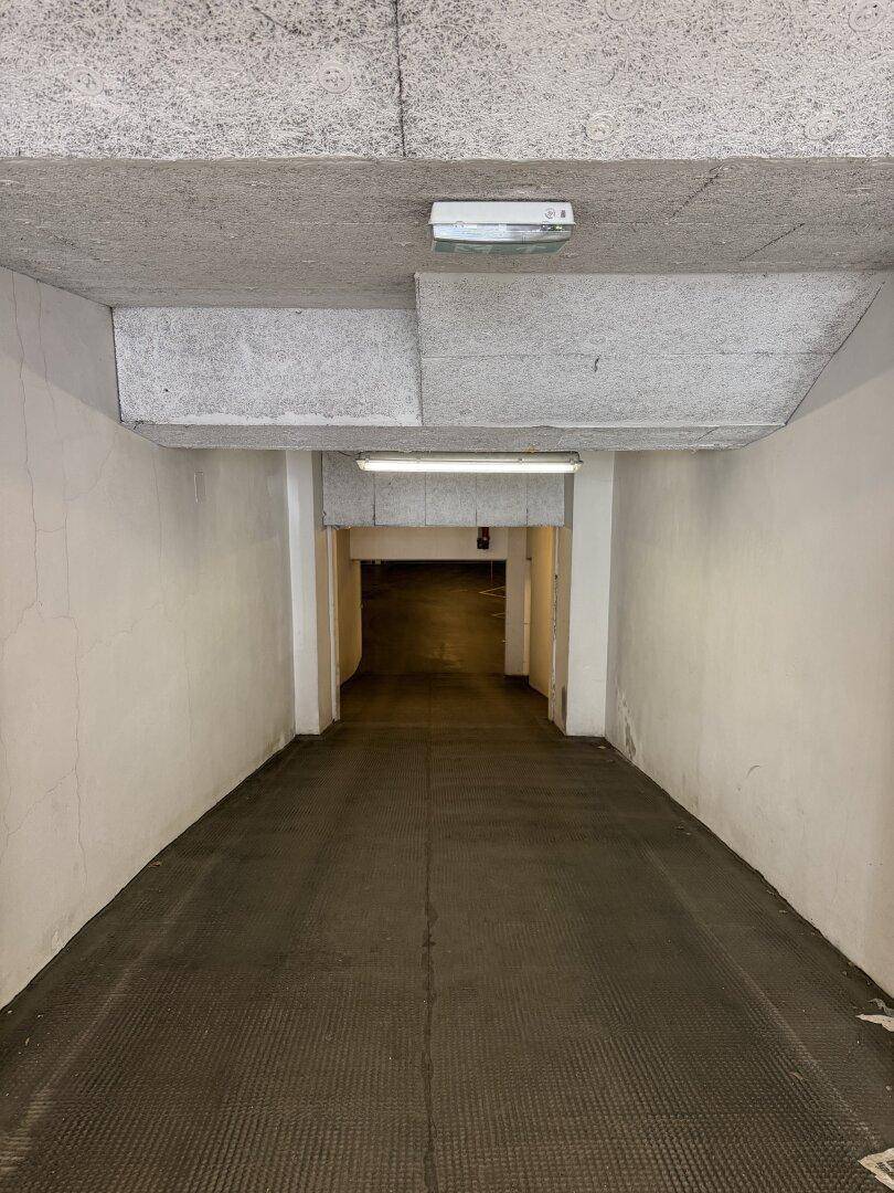 Einfahrt zu einer Tiefgarage mit Betonwänden und Decke, die in den dunklen Parkbereich führt.