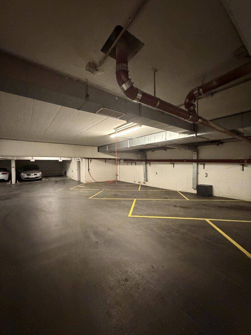 Geräumige Tiefgarage mit markierten Stellplätzen, sichtbaren Rohren und Lüftungskanälen an der Decke.