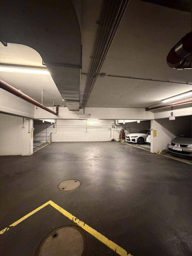 Tiefgarage mit geparkten Fahrzeugen und klar markierten Stellplätzen unter sichtbaren Deckeninstallationen.